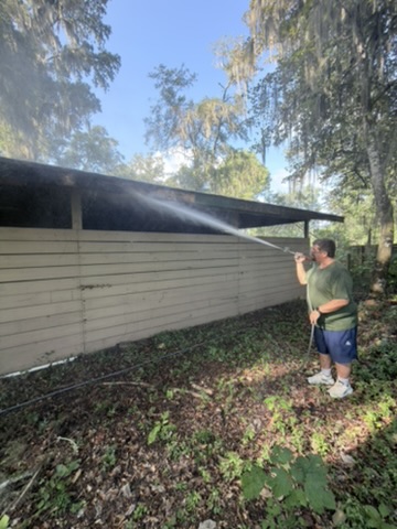 UPPW technician spraying the upper exterior of a pale wood barn beneath moss-draped trees in Ocala