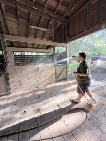 UPPW technician washing a wood stall front beneath green metal bars inside an Ocala barn