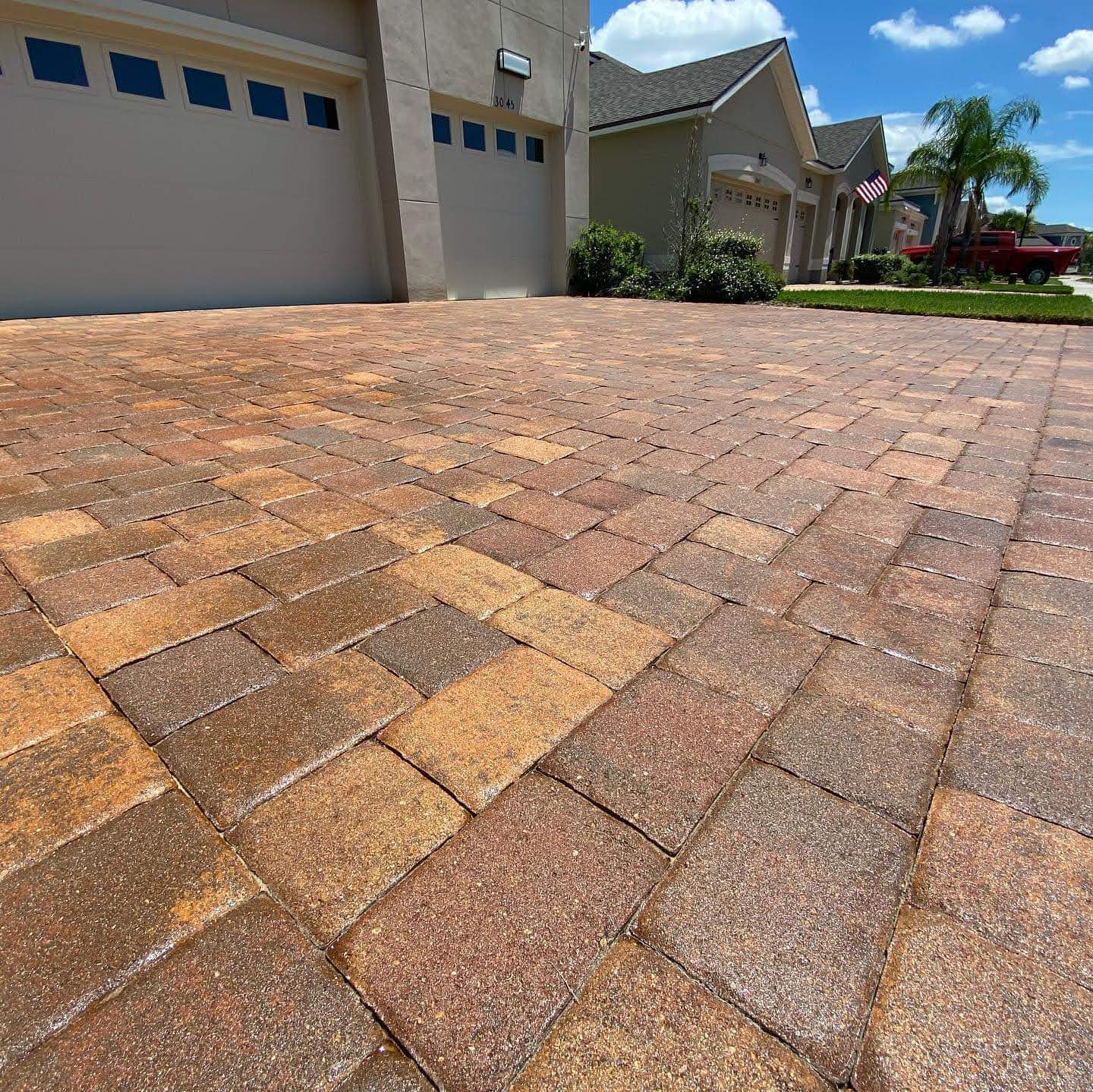 Tan, rust, and charcoal driveway pavers in front of a light-colored home, photographed from a low angle.